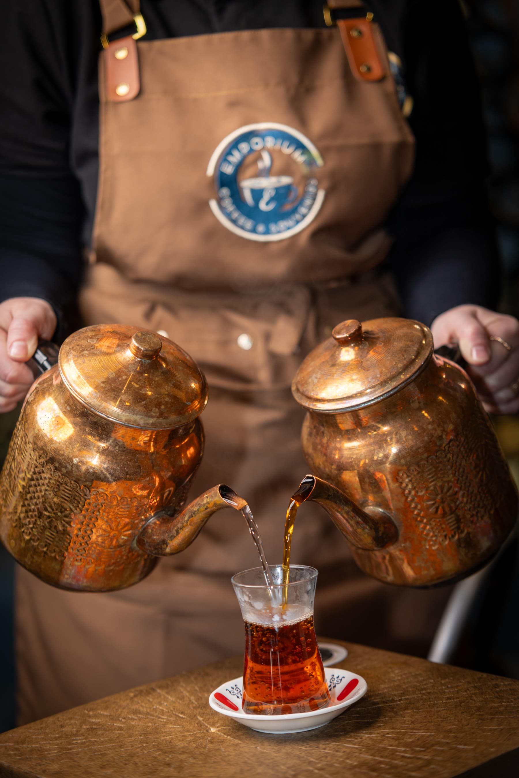Barista pouring Turkish tea from two copper teapots at Emporium