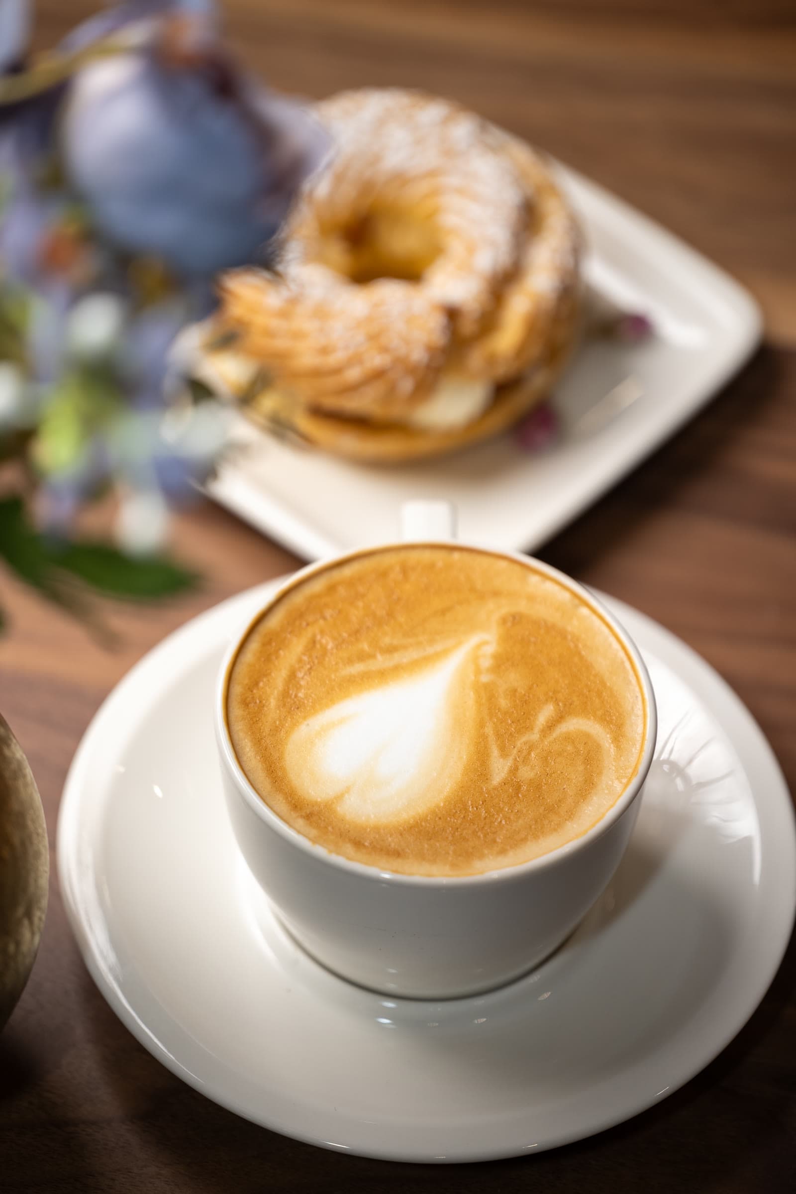 Cream-filled cruller pastry beside a latte with leaf-pattern latte art