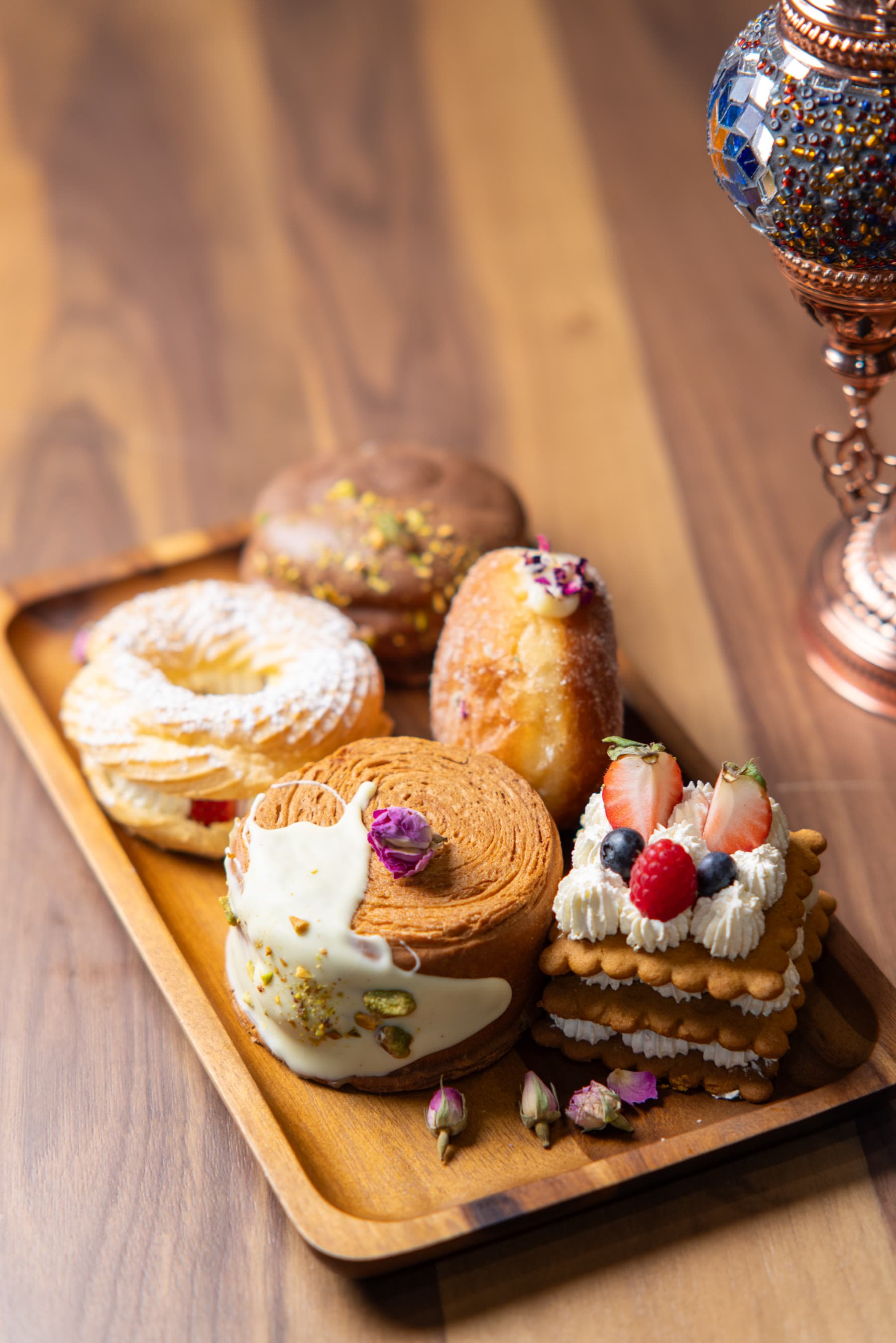 Wooden tray of assorted pastries: chocolate pistachio donut, cruller, mille-feuille, and berry stack